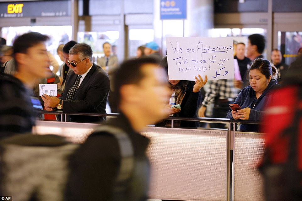 Attorney Sabra Gandhi holds up a sign while travelers pass by as protests against President Donald Trump's executive order banning travel from seven Muslim-majority countries continue at Los Angeles International Airport