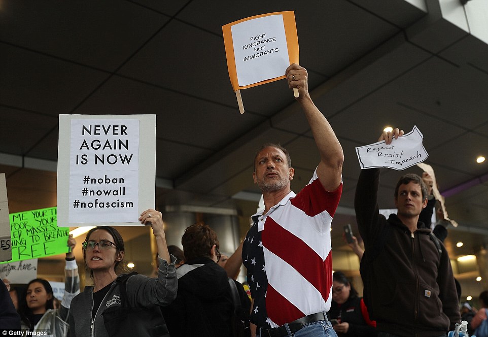 A man wearing a Stars And Stripes shirt joined the protest at Miami International Airport while holding a sign that read: 'Fight ignorance not migrants'
