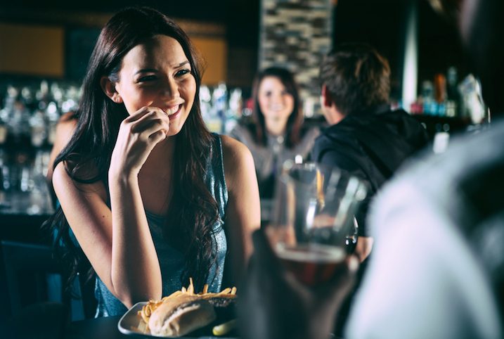 couple at a bar having drinks while the woman laughs at the table