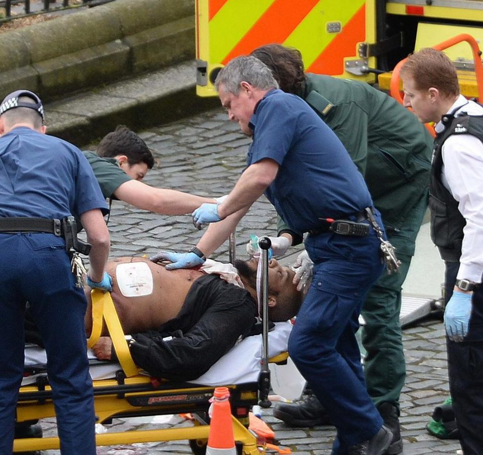 The suspect lies on a stretcher outside Parliament with paramedics treating his injuries while armed cops stand guard